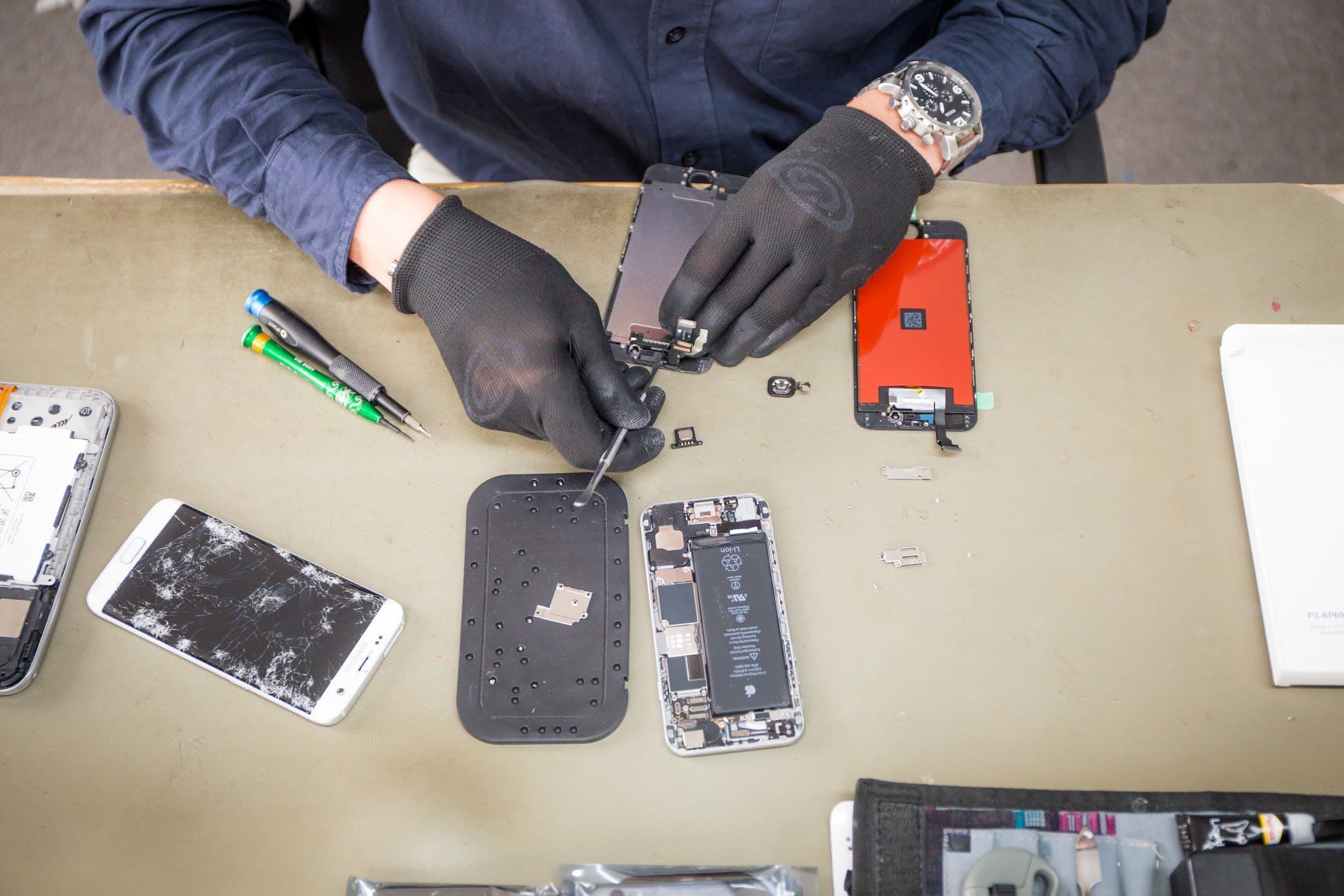 A repairer taking a phone apart at the workbench, parts and tools laid out around it